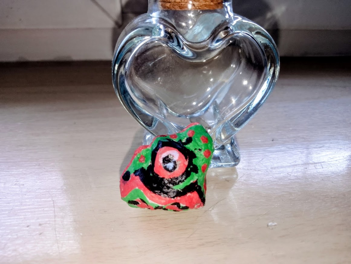 Głowa dinozaura namalowana na kamieniu – czarno-czerwono-zielona